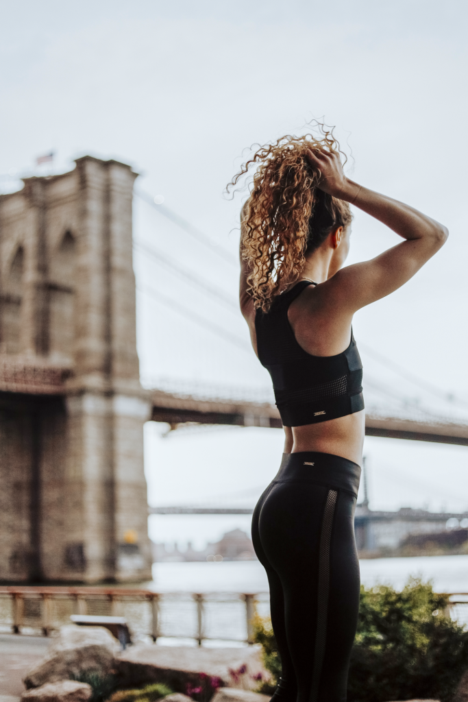 Woman in workout clothes puts her curly hair in a ponytail.