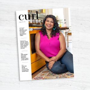 aarti sequeira wears her curly hair while sitting on the floor and smiling in front of her yellow kitchen oven