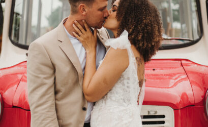 A curly-haired bride wearing her natural hair down kisses her groom in front of a vintage ice cream truck